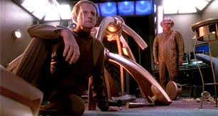 Odo sitting in the mess that is now his quarters and Quark standing in his pajamas