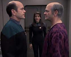 Troi looks on as the EMH and Dr. Zimmerman stare at each other